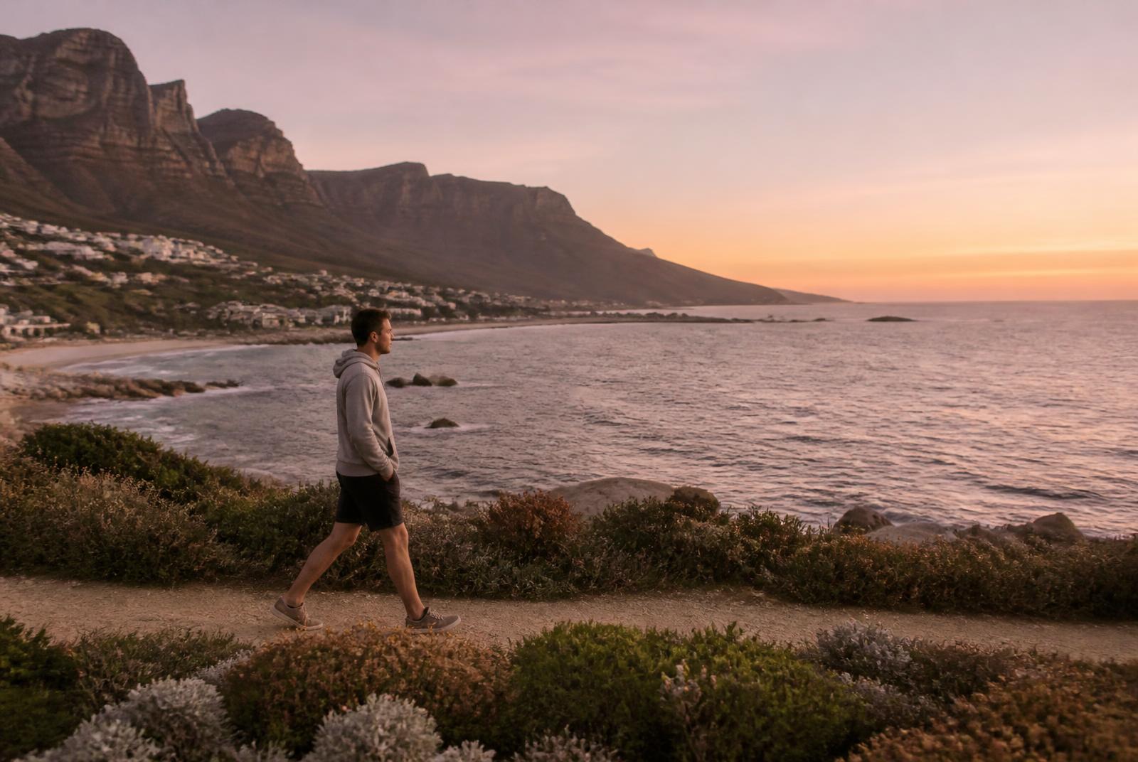Man walking a Cape Town coastal path at dusk with his phone left behind, practising a healthier response to stress